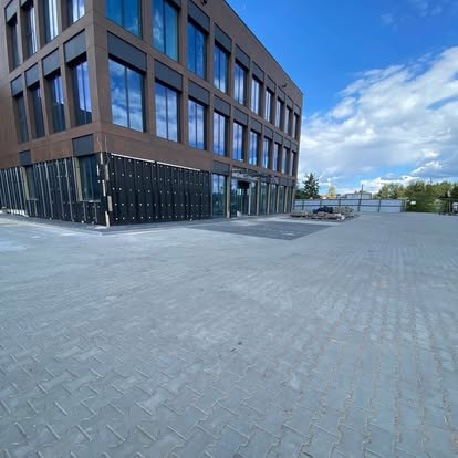 Nowoczesny budynek biurowy z kostką brukową na dziedzińcu, błękitne niebo z chmurami w tle. Widok z niskiej perspektywy.