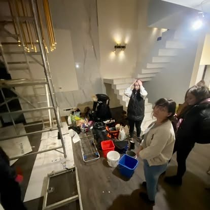 Ekipa sprzątająca w trakcie pracy w przestronnym wnętrzu z marmurowymi ścianami i schodami. Na podłodze widoczne narzędzia i akcesoria do sprzątania.