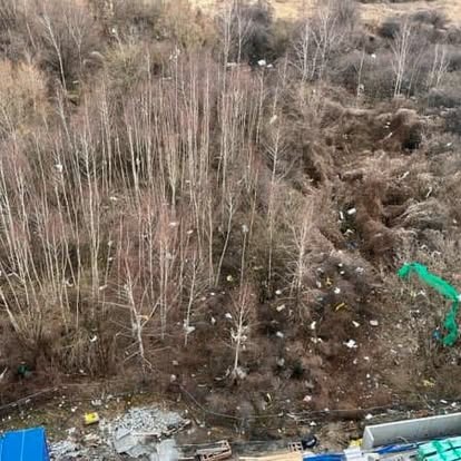 Widok z góry na teren zanieczyszczony śmieciami, częściowo porośnięty drzewami. W tle widoczne budynki i błękitne plandeki.