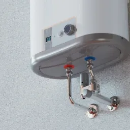 Nowy podgrzewacz wody z chromowanymi rurami podłączony do ściany w Kołobrzegu, widoczne złącza oznaczone kolorami niebieskim i czerwonym.