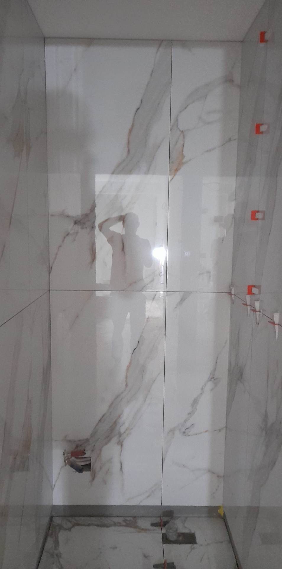 Montaż płytek imitujących marmur na ścianie, widoczne krzyżyki dystansowe, odbicie osoby w płytkach, częściowo ułożona podłoga.