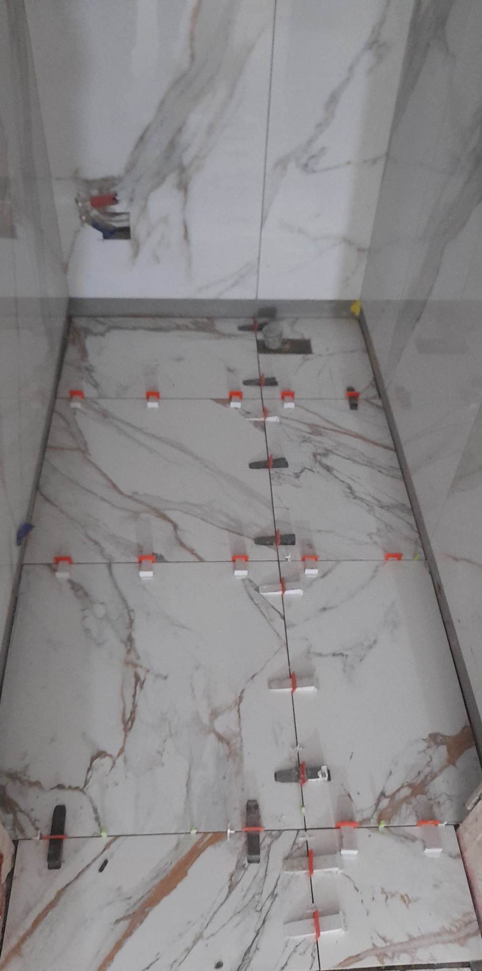 Układanie białych płytek imitujących marmur z użyciem systemów poziomowania płytek w trakcie remontu łazienki.