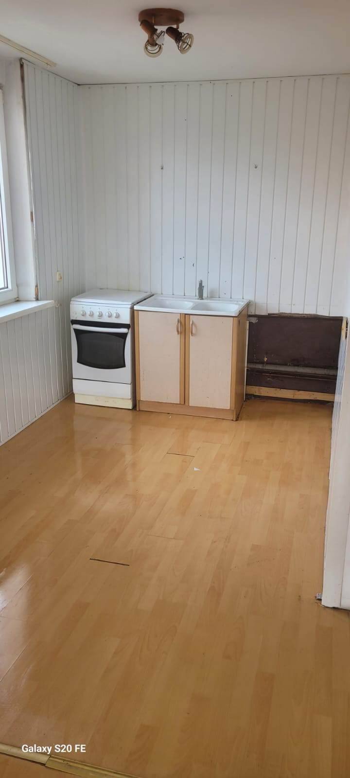 Wnętrze pokoju przed remontem z piecem, szafką z umywalką i odsłoniętą instalacją pod ścianą, drewniana podłoga