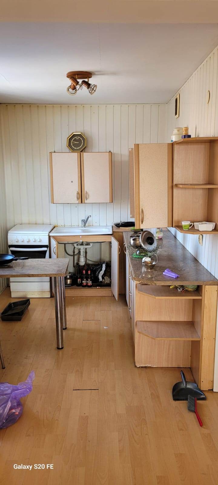 Wnętrze kuchni przed remontem z widocznymi starymi meblami, zlewem, kuchenką i nieporządkiem na podłodze, zarysowaniami na ścianach i brakiem estetyki.