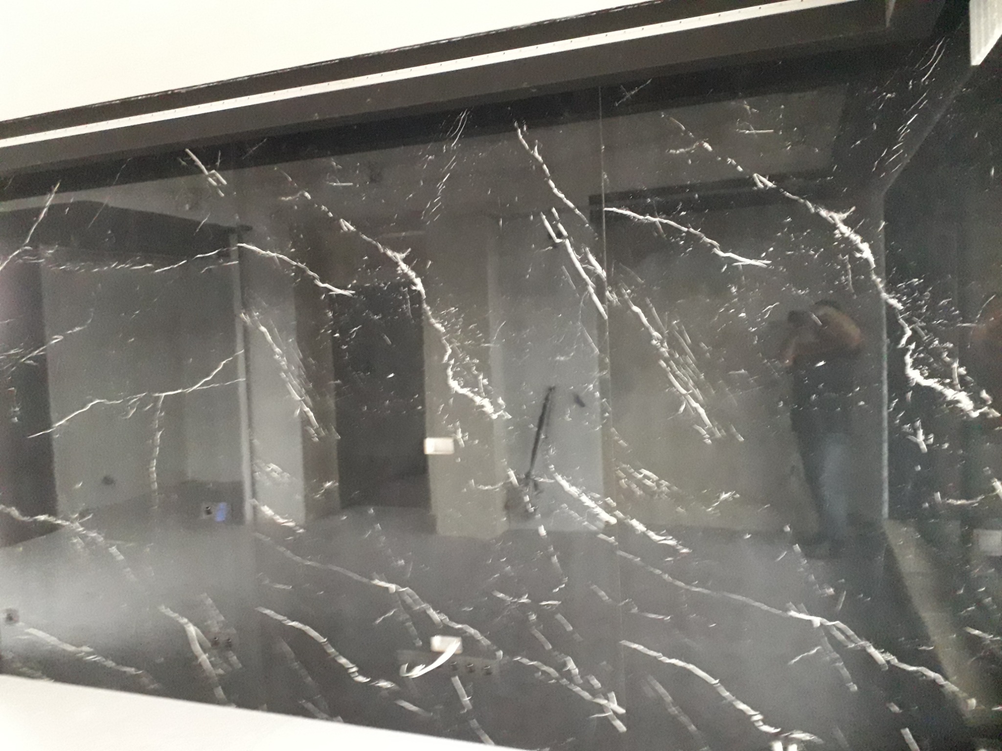 Ciemna, błyszcząca ściana z płytek imitujących marmur z wyraźnym, białym żyłkowaniem; widoczne odbicie osoby w lustrzanej powierzchni płytek.