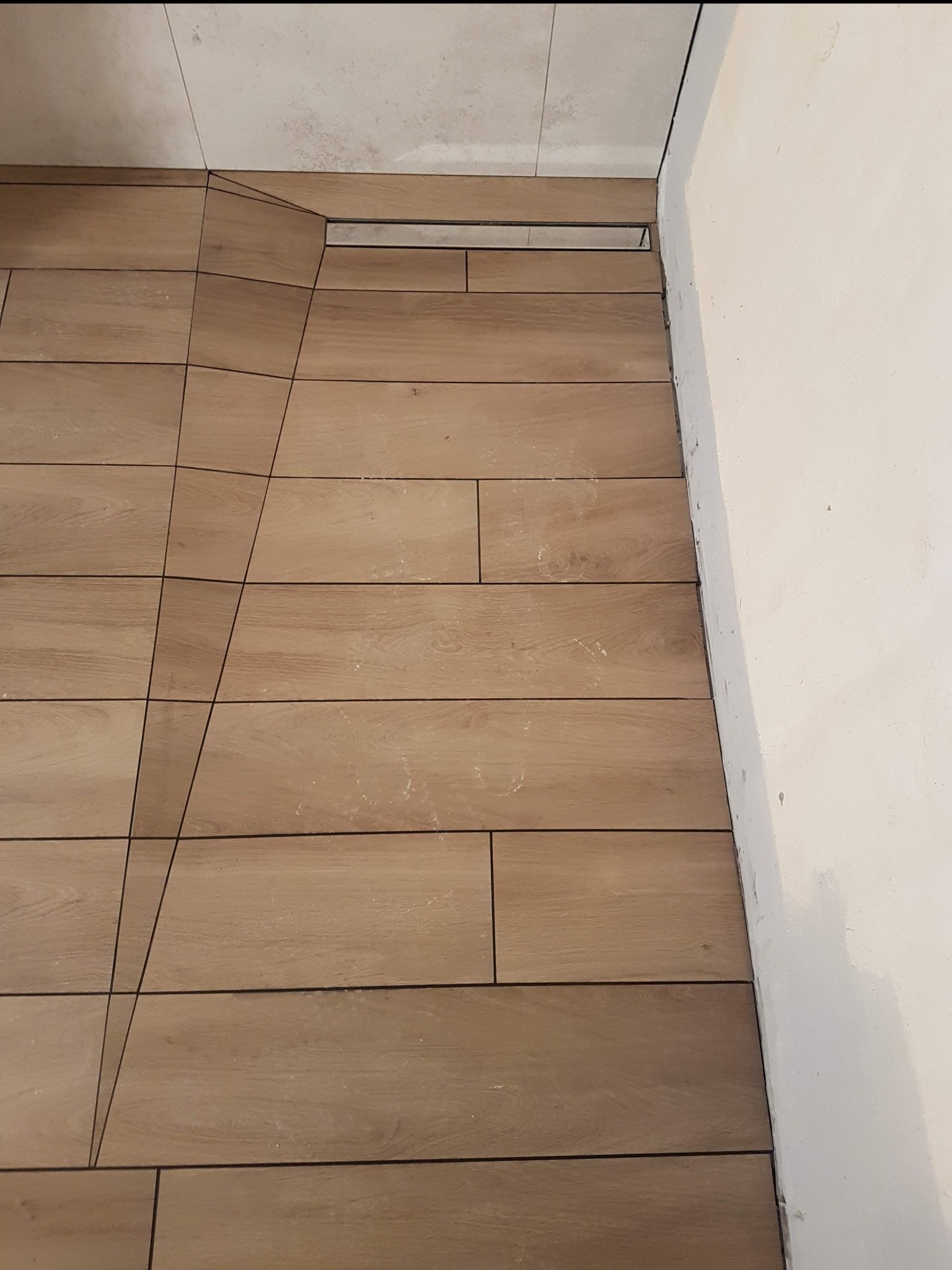 Ukończona podłoga w łazience z płytek imitujących drewno, z odpływem liniowym przy ścianie, widoczne niedoskonałości na styku ściany i podłogi.