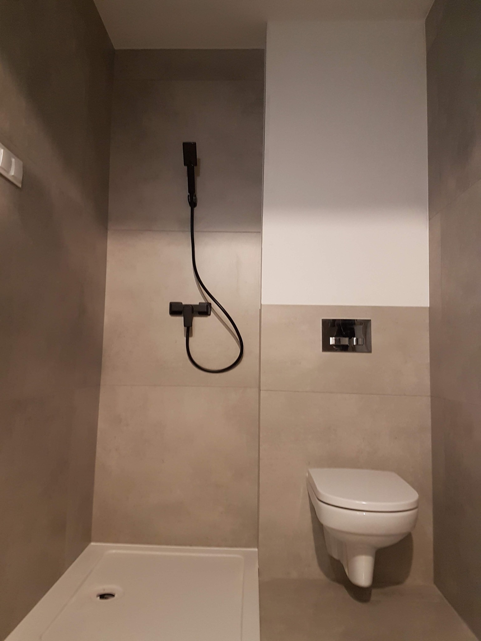 Nowoczesna łazienka z kabiną prysznicową typu walk-in i podwieszaną toaletą, wykończona płytkami w odcieniach beżu i szarości, z czarną armaturą.