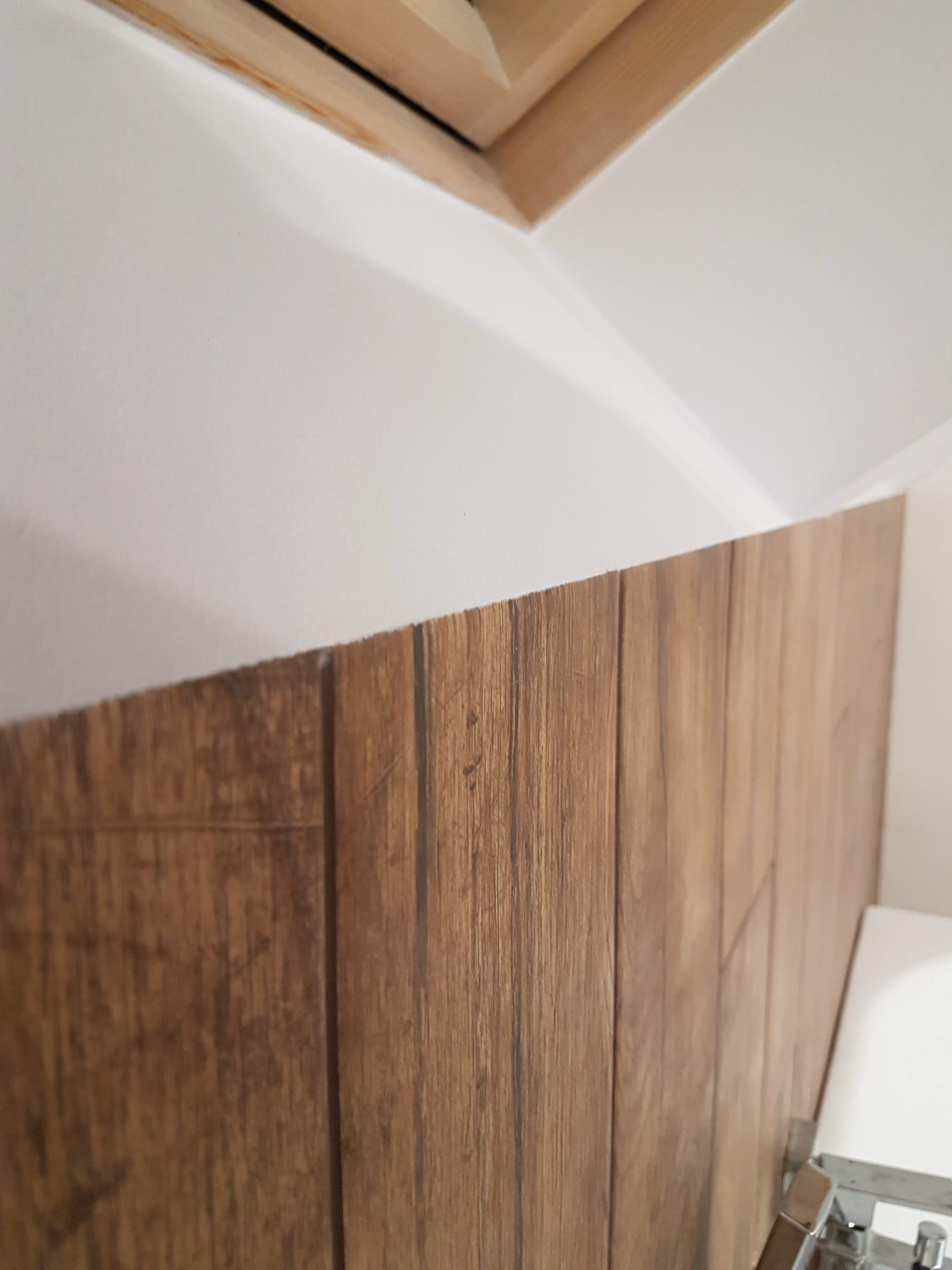 Fragment ściany wykończonej panelami drewnopodobnymi w łazience, widoczny fragment sufitu i armatury.