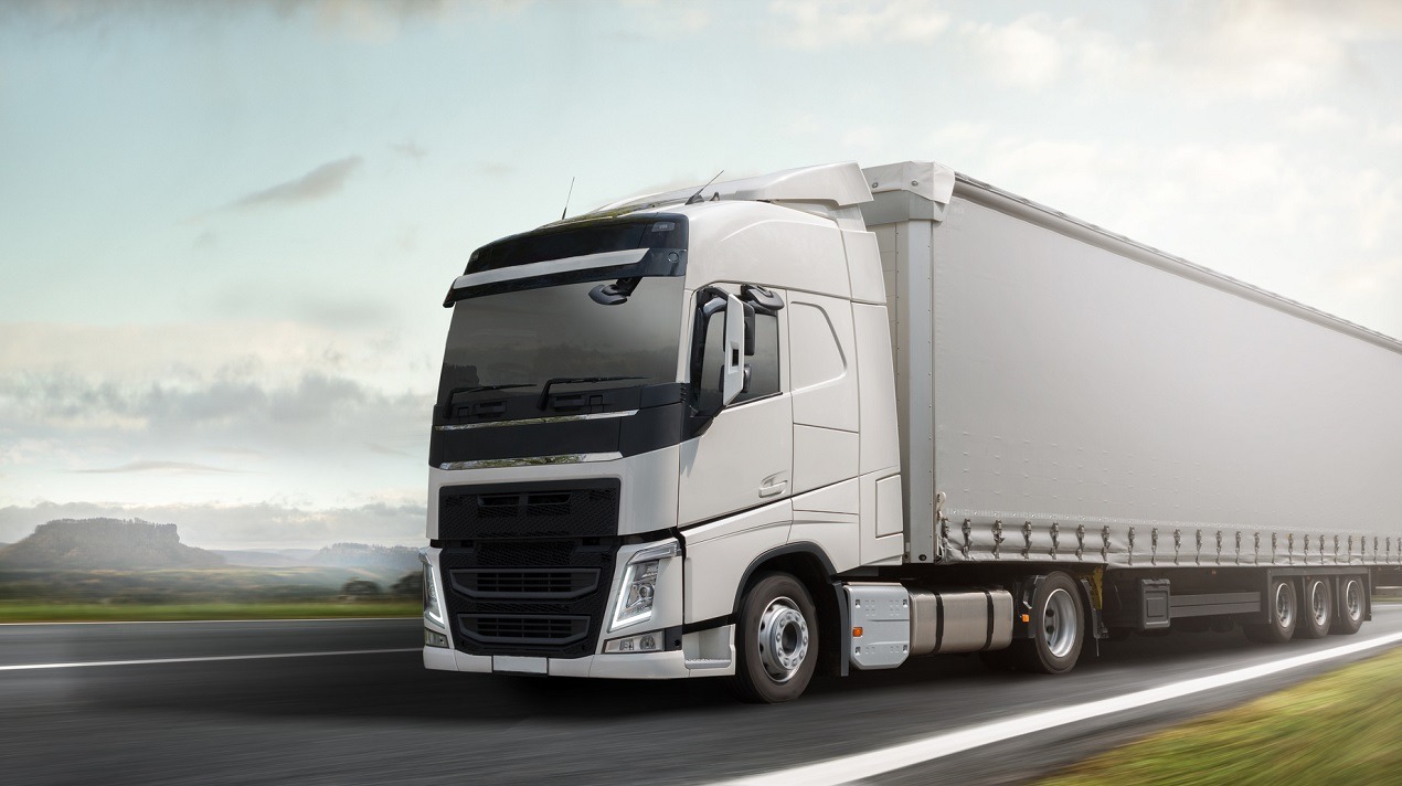 Biała ciężarówka z naczepą w ruchu na autostradzie, widok z boku, z rozmytym tłem krajobrazu.