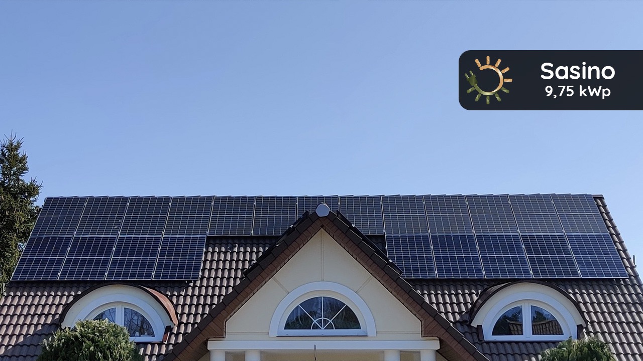 Panele słoneczne na brązowym dachu domu z oknami w kształcie półksiężyca, widoczne logo firmy Sasino 9,75 kWp.