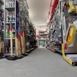 Wnętrze sklepu budowlanego z perspektywy podłogi, ukazujące rzędy półek wypełnionych narzędziami i materiałami, w tym młotki z drewnianymi trzonkami i różnorodne akcesoria montażowe.