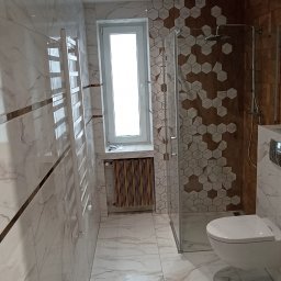 Usługi remontowo-budowlane Team Daniel's - Wykończona łazienka z kabiną prysznicową, toaletą i grzejnikiem drabinkowym. Płytki imitujące marmur na ścianach i podłodze, dekoracyjne heksagony pod prysznicem.