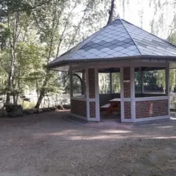 Altana z dachem krytym szarą dachówką karpiówką, w tle widok na jezioro i drzewa.