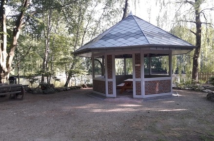 Altana z dachem krytym szarą dachówką karpiówką, w tle widok na jezioro i drzewa.