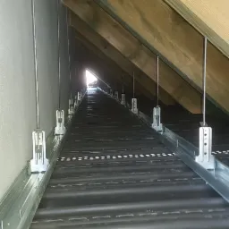 Konstrukcja metalowa z wieszakami przymocowana do krokwi dachowych, przygotowana pod ocieplenie poddasza, widok w perspektywie z głąbi strychu w kierunku okna.