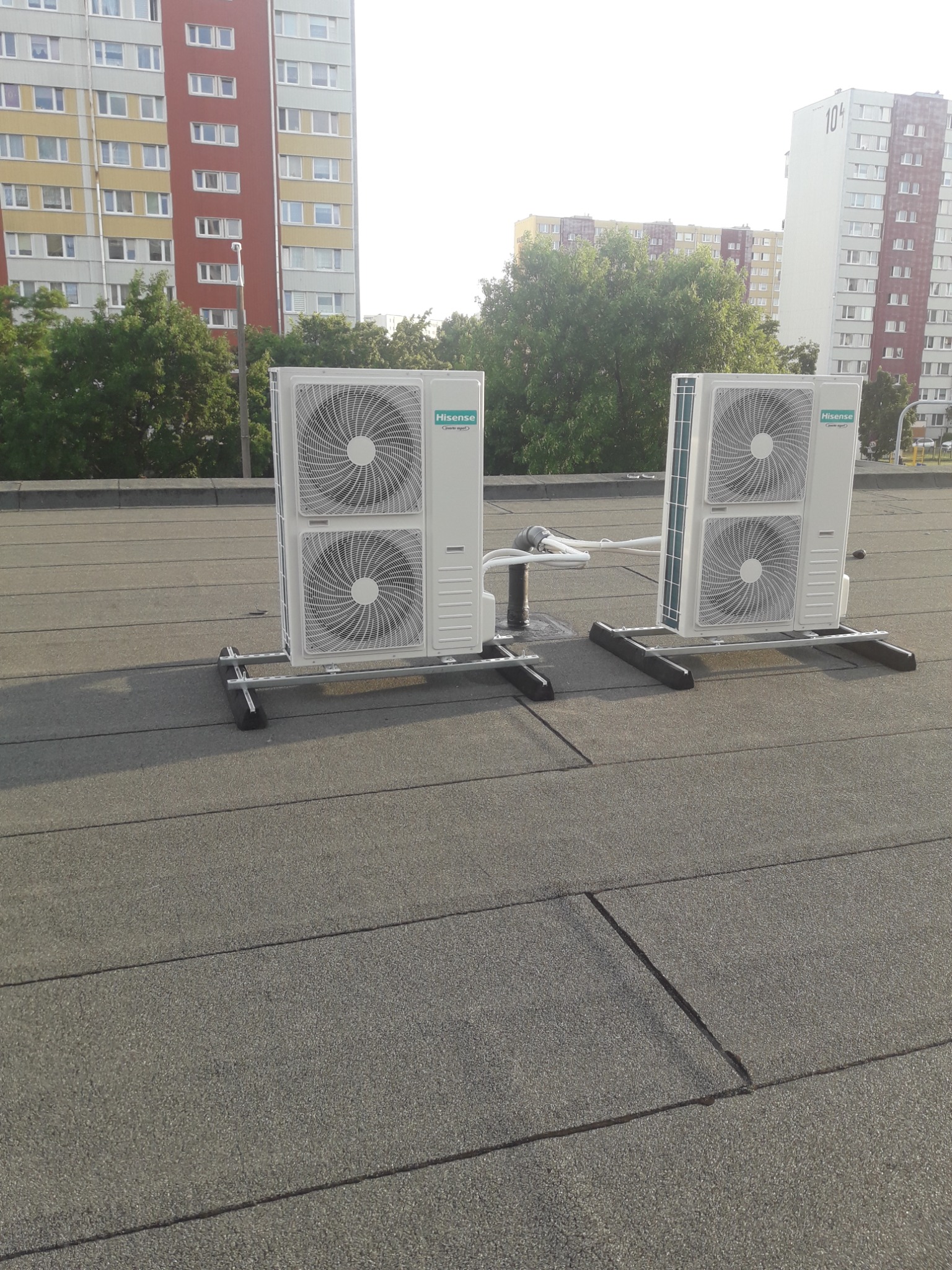 Dwa białe klimatyzatory marki Hisense zamontowane na dachu budynku, widoczne bloki mieszkalne w tle.
