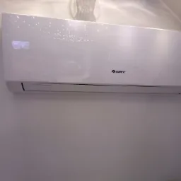 Biała jednostka wewnętrzna klimatyzatora marki Gree zamontowana na ścianie w pomieszczeniu z niebieskim sufitem i punktowym oświetleniem.