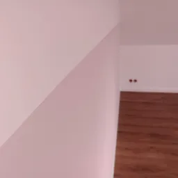 Świeżo pomalowane na różowo wnętrze z drewnianą podłogą, widoczne gniazdka elektryczne w ścianie.