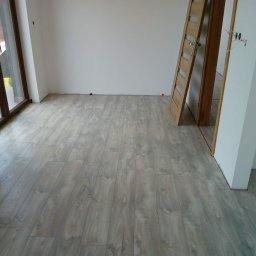 Sucha zabudowa , szpachlowanie , malowanie , podłogi, laminat, winyl - Nowo położona podłoga laminowana w odcieniach szarości, widoczne drzwi wewnętrzne z drewnianą ościeżnicą, ściany przygotowane pod malowanie, surowy stan wykończenia wnętrza.