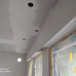 Sucha zabudowa , szpachlowanie , malowanie , podłogi, laminat, winyl - Szpachlowany sufit z widocznymi otworami na oświetlenie, okna zabezpieczone folią malarską, widoczne ślady szpachli.