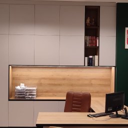 BPM Bujanowski Pracownia Mebli - Biuro z szarymi szafami na wymiar z drewnianymi elementami, biurkiem z komputerem i fotelem, na ścianie godło Polski.
