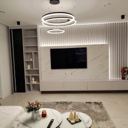 BPM Bujanowski Pracownia Mebli - Nowoczesny salon z marmurową ścianą TV, podświetlanymi lamelami, okrągłymi lampami i dekoracjami świątecznymi na stolikach kawowych.
