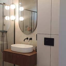 BPM Bujanowski Pracownia Mebli - Nowoczesna łazienka z owalną umywalką nablatową na drewnianej szafce, wisząca toaleta i podświetlane lustro owalne, oświetlenie kuliste, armatura w kolorze czarnym, beżowe płytki.