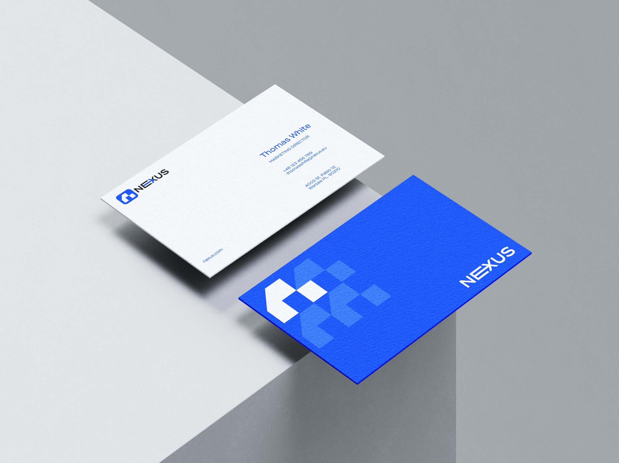 Dwie wizytówki firmy Nexus, jedna biała z niebieskim logo i danymi kontaktowymi, druga niebieska z białym logo, ułożone pod kątem na szarym tle.