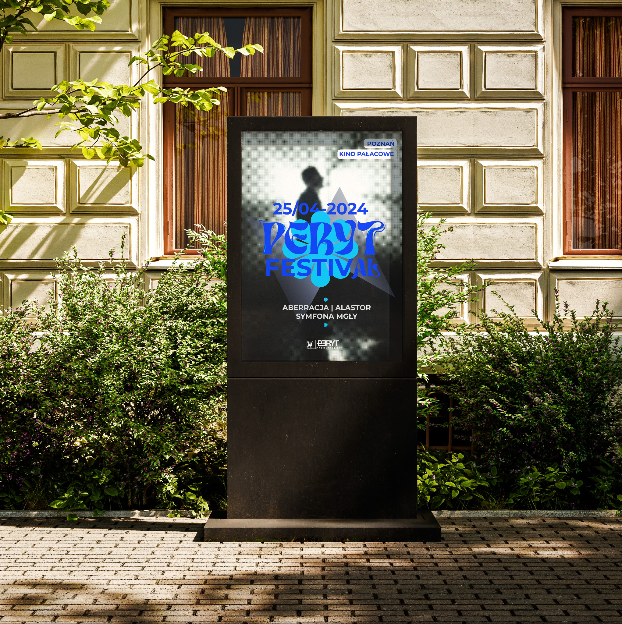 Billboard reklamowy przed budynkiem kina Pałacowe w Poznaniu, promujący Peryt Festiwal, otoczony zielenią.