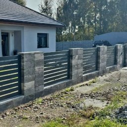 Spec-stal - Nowoczesne ogrodzenie z szarego kamienia łupanego i poziomych, metalowych przęseł, otaczające dom z białymi ścianami i ciemną dachówką. Tło: drzewa i błękitne niebo.