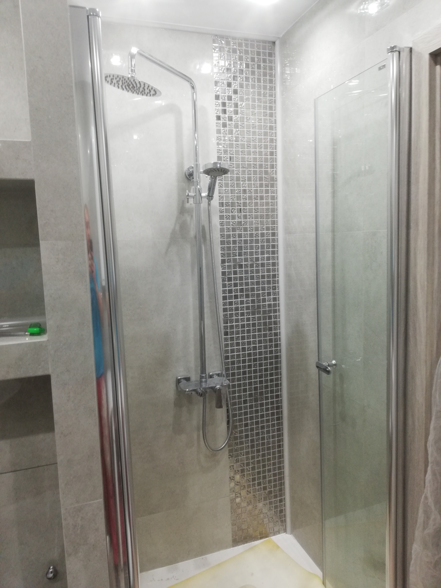 Nowoczesna kabina prysznicowa z deszczownicą i mozaiką w strefie natrysku, widok na szklane drzwi i chromowaną armaturę.