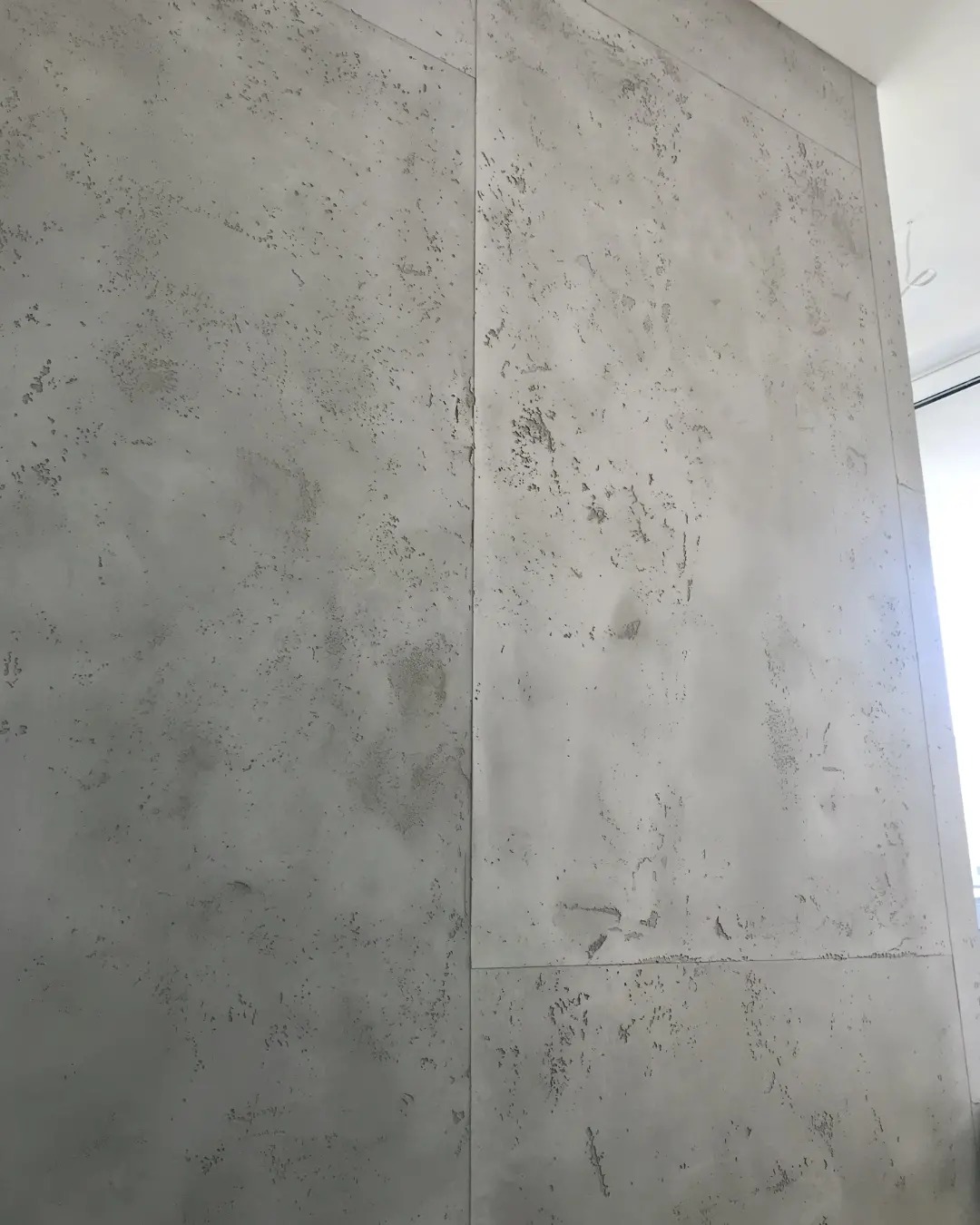 Szara ściana wykończona szpachlą dekoracyjną imitującą beton, podzielona na panele, widoczne łączenia.