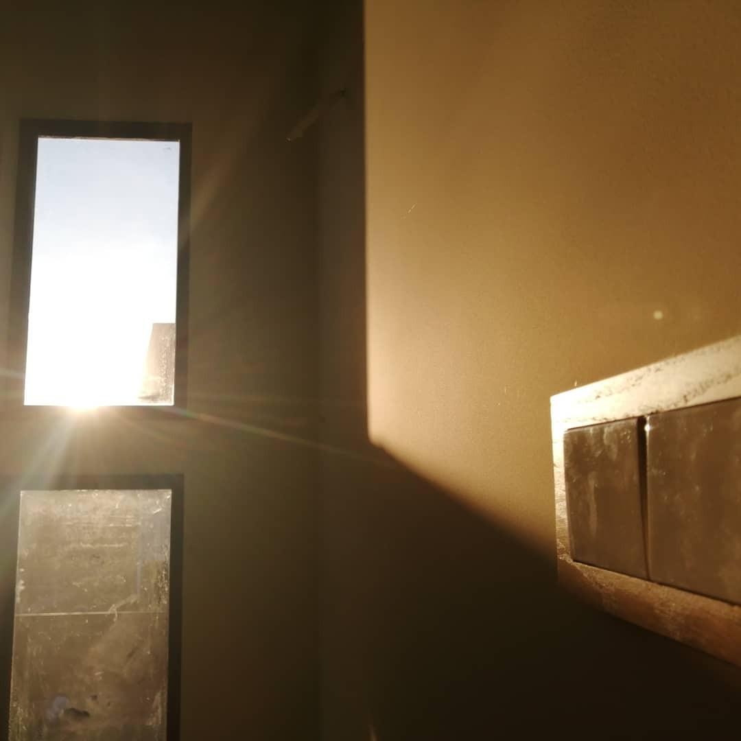 Światło słoneczne wpadające przez okno na świeżo pomalowaną ścianę w odcieniach brązu, widoczne włączniki światła z ramką.