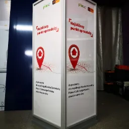 Trójstronny, wolnostojący pylon reklamowy z logo Plus i mapą wskazującą najbliższy punkt sprzedaży, umieszczony na szarym cokole.