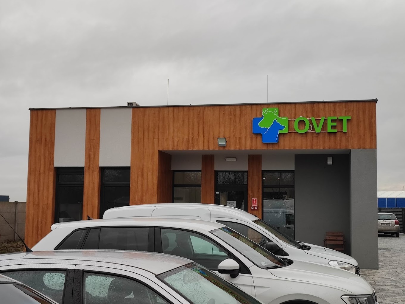 Budynek kliniki weterynaryjnej TOVET z logo przedstawiającym zielonego konia i niebieskiego psa w krzyżu, widoczne zaparkowane samochody na pierwszym planie.