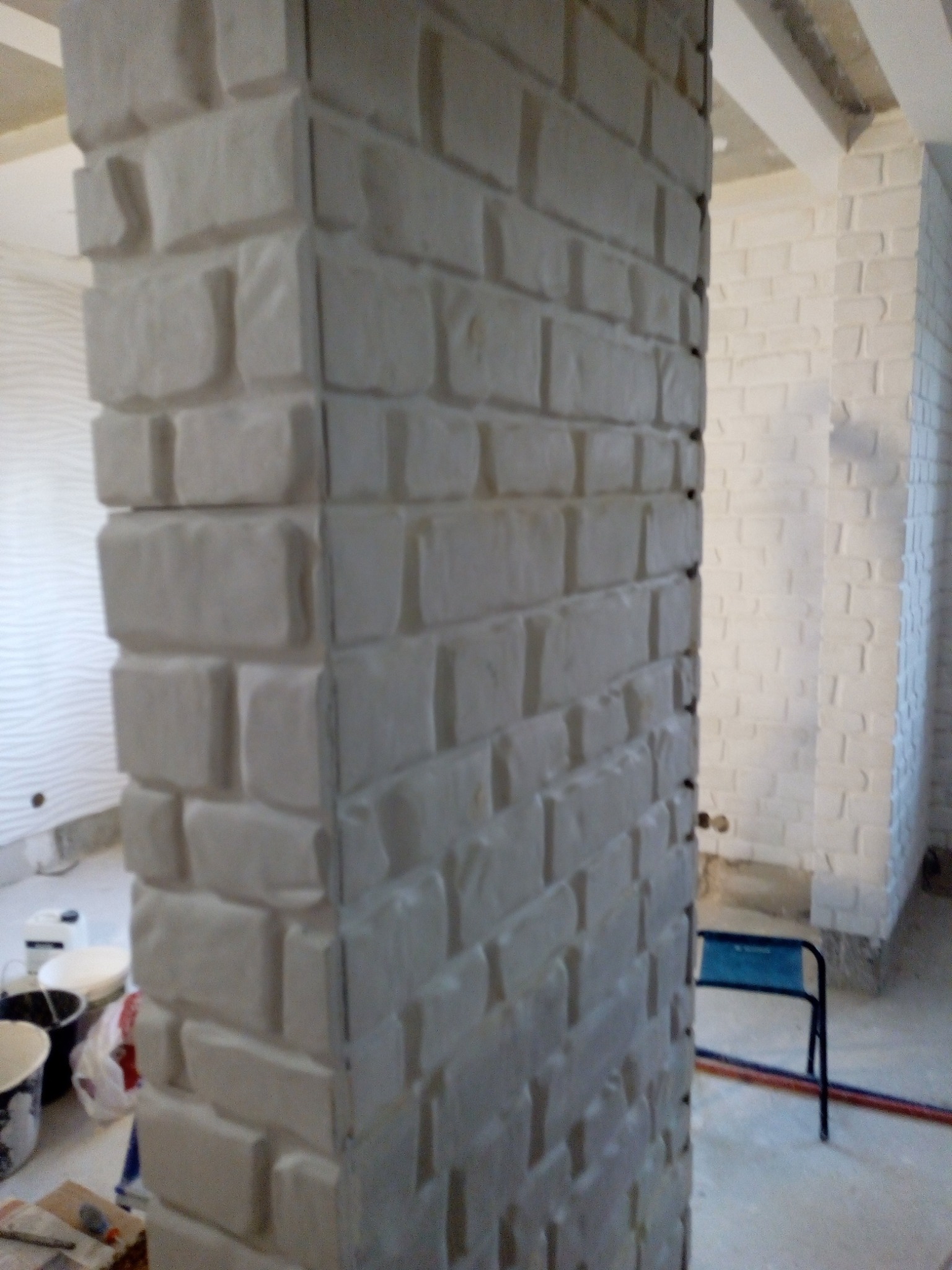 Kolumna z dekoracyjnej, białej cegły w Pruszkowie, z widocznymi śladami prac wykończeniowych na podłodze i ścianach w tle.