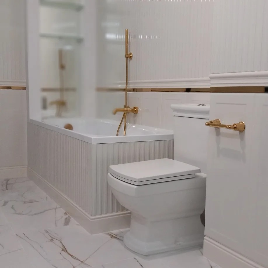 Biała łazienka z wanną, toaletą i złotymi detalami, marmurowa podłoga.