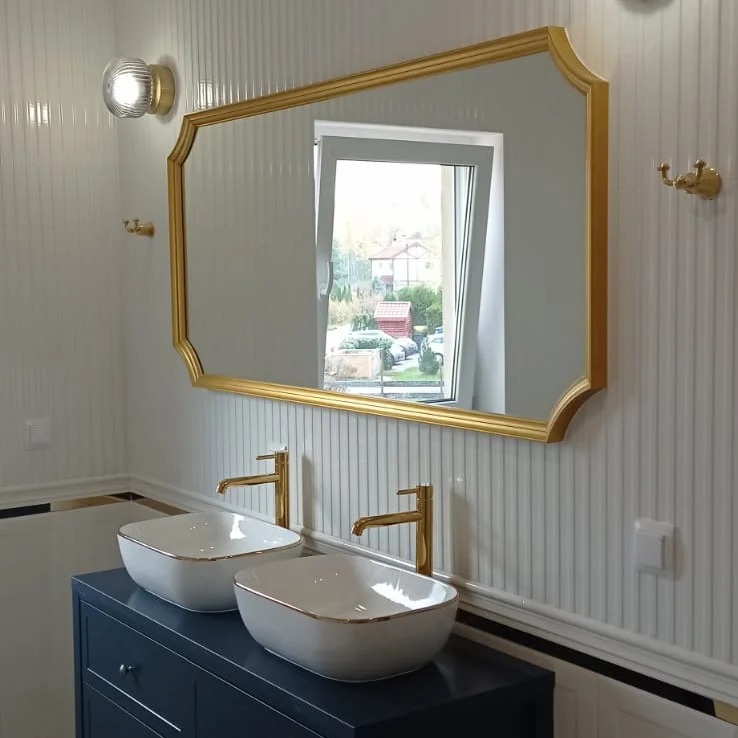 Łazienka z dwoma umywalkami nablatowymi, złotą armaturą i lustrem w złotej ramie, na tle ściany w pionowe paski.
