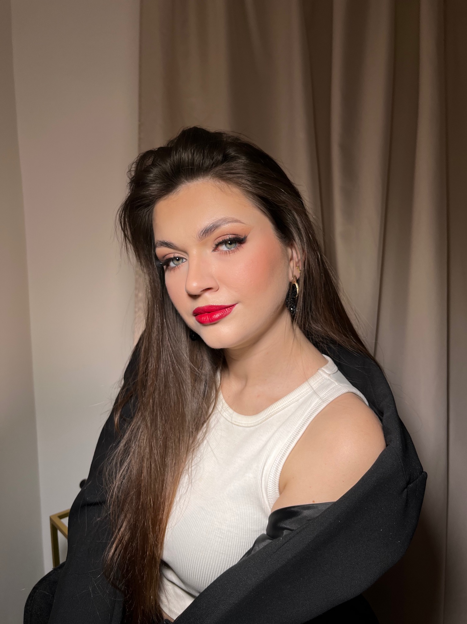 Portret kobiety z błyszczącym makijażem oczu i ustami w kolorze głębokiej czerwieni. Uwagę przykuwają długie, ciemne kolczyki.