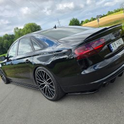 SPEED HADI TAXI MATEUSZ HADAŁA - Czarny, zmodyfikowany samochód osobowy Audi A8 z polską tablicą rejestracyjną R8 HAD1, zaparkowany na asfaltowej drodze w wiejskim otoczeniu z polami i drzewami w tle.