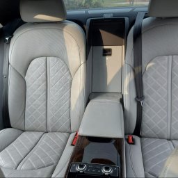 SPEED HADI TAXI MATEUSZ HADAŁA - Wnętrze luksusowego samochodu z jasną, skórzaną tapicerką siedzeń o wzorze rombów, widok na tylną kanapę z podłokietnikiem i panelem sterowania klimatyzacją.