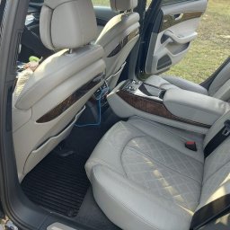 SPEED HADI TAXI MATEUSZ HADAŁA - Jasnoszara, skórzana tapicerka tylnych siedzeń luksusowego samochodu z drewnianymi elementami wykończenia i widocznym kablem USB.