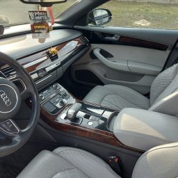 SPEED HADI TAXI MATEUSZ HADAŁA - Wnętrze samochodu Audi A8 z jasną skórzaną tapicerką, drewnianymi wykończeniami i zawieszką 'Pokaz Driftu' na lusterku.