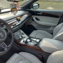 Wnętrze samochodu Audi A8 z jasną skórzaną tapicerką, drewnianymi wykończeniami i zawieszką 'Pokaz Driftu' na lusterku.