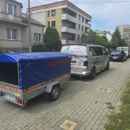 SPEED HADI TAXI MATEUSZ HADAŁA - Przyczepa z niebieską plandeką zaparkowana na chodniku obok srebrnego busa z reklamą ośrodka wypoczynkowego i numerem telefonu.