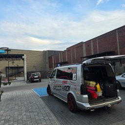 SPEED HADI TAXI MATEUSZ HADAŁA - Srebrny van z otwartym bagażnikiem, wypełnionym bagażami, zaparkowany na parkingu z kostki brukowej przed budynkiem.