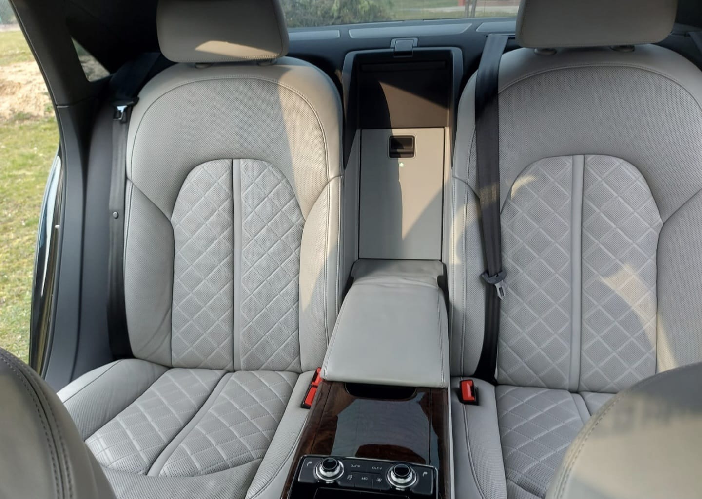 Wnętrze luksusowego samochodu z jasną, skórzaną tapicerką siedzeń o wzorze rombów, widok na tylną kanapę z podłokietnikiem i panelem sterowania klimatyzacją.