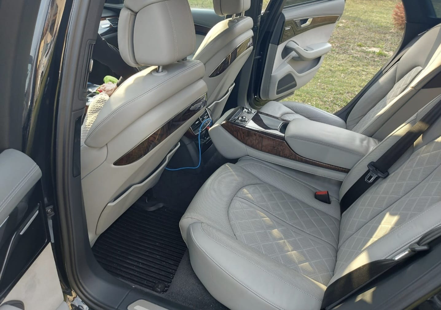 Jasnoszara, skórzana tapicerka tylnych siedzeń luksusowego samochodu z drewnianymi elementami wykończenia i widocznym kablem USB.