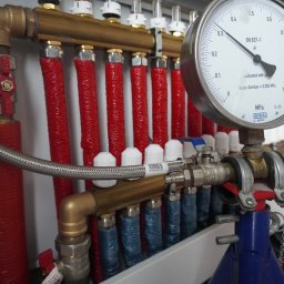 HYDRAKO Sławomir Kowal - Rozdzielacz ogrzewania podłogowego z manometrem WIKA, rurami w izolacji czerwonej i niebieskiej. Czerwony obcinak do rur w tle. Widok z bliska na instalację.