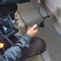 HYDRAKO Sławomir Kowal - Pracownik w kombinezonie sprawdza szczelność instalacji gazowej za pomocą specjalistycznego urządzenia diagnostycznego. Widoczny ekran z wykresem.
